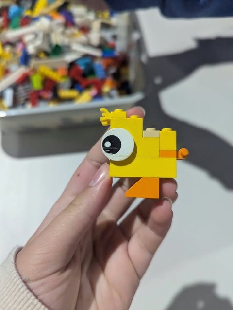 A small yellow brick-built duck held up in front of a tub of loose LEGO
