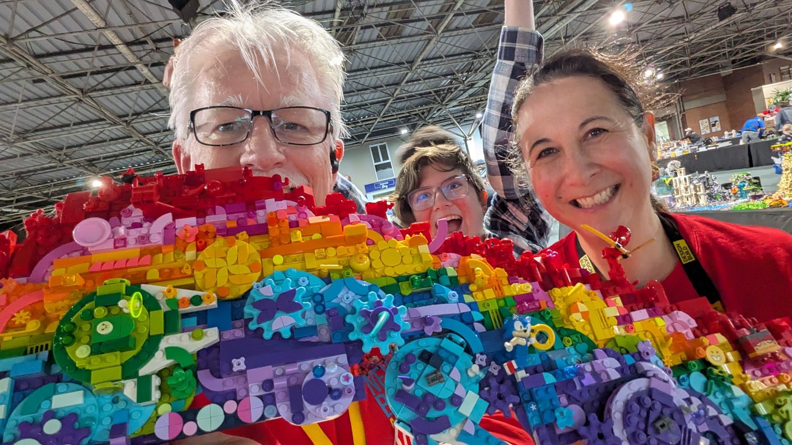 Smiling Rainbow Bricks team members holding up a colourful rainbow LEGO build
